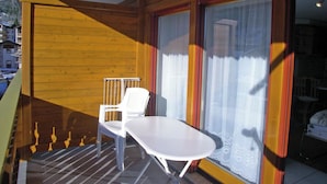 En balkon med en hvid stol og et bord, trævægge og udsigt udad.