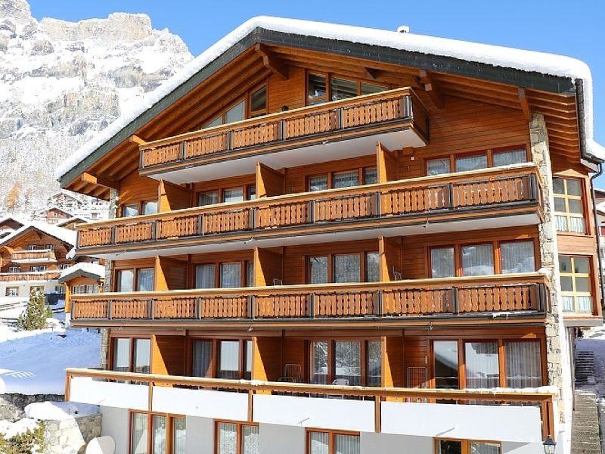 Un edificio de madera de varios pisos con balcones, con una imponente montaña nevada al fondo.