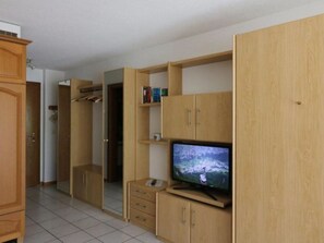 Ein Zimmer mit Fernseher auf einem Holzgestell, einem Kleiderschrank und einem Spiegel.