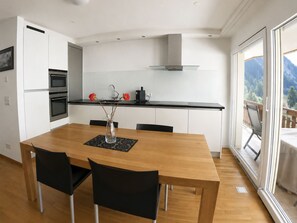 Eine moderne Küche mit weißen Schränken, einer schwarzen Arbeitsplatte und einem Essbereich mit einem Holztisch und schwarzen Stühlen.