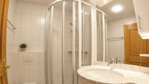 Ett modernt badrum med en duschavdelning med glasväggar, en vit toalett och ett handfat i marmor.