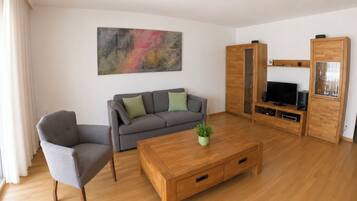 Ein modernes Wohnzimmer mit grauem Sofa, einem Holztisch und einem Fernsehmöbel.