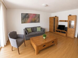 A modern living room with a grey sofa, a wooden coffee table, and a TV stand. - Residenz Edelweiss Leukerbad # 3-bed apartment, Dusche, WC by Interhome (Leukerbad)