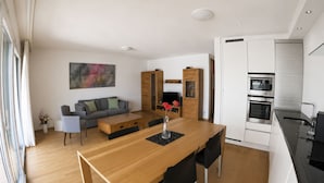 Ett modernt kök med vita skåp, ett matbord i trä med svarta stolar och en inbyggd ugn.