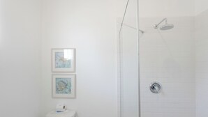 Un bagno con un water, due quadri appesi al muro e uno spazio doccia con soffione.