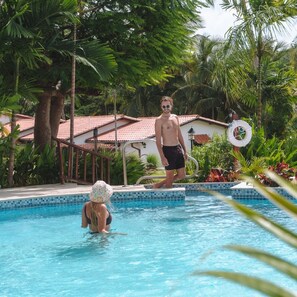 A swimming pool with a tiled edge, surrounded by lush greenery and a building with a red-tiled roof. - 2 bed Ocean View apartment  in Speightstown - Sand Dollar, Sand Street apt 1 (Speightstown)