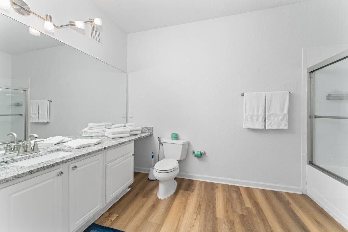 A bathroom with a white sink, toilet, and shower, with white towels and a mirror.