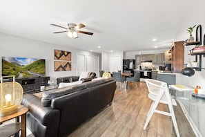 A modern living room with a black leather sofa, a dining area with a white chair, and a kitchen with wooden cabinets. - Switchback Suites - Side B (Bentonville)