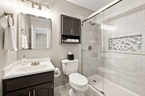 A modern bathroom with a glass shower enclosure, a vanity with a sink, a toilet, and a mirror. - Switchback Suites - Side B (Bentonville)
