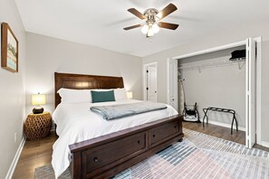 A bedroom with a bed, bedside lamp, wooden headboard, ceiling fan, and a walk-in closet. - Switchback Suites - Side B (Bentonville)