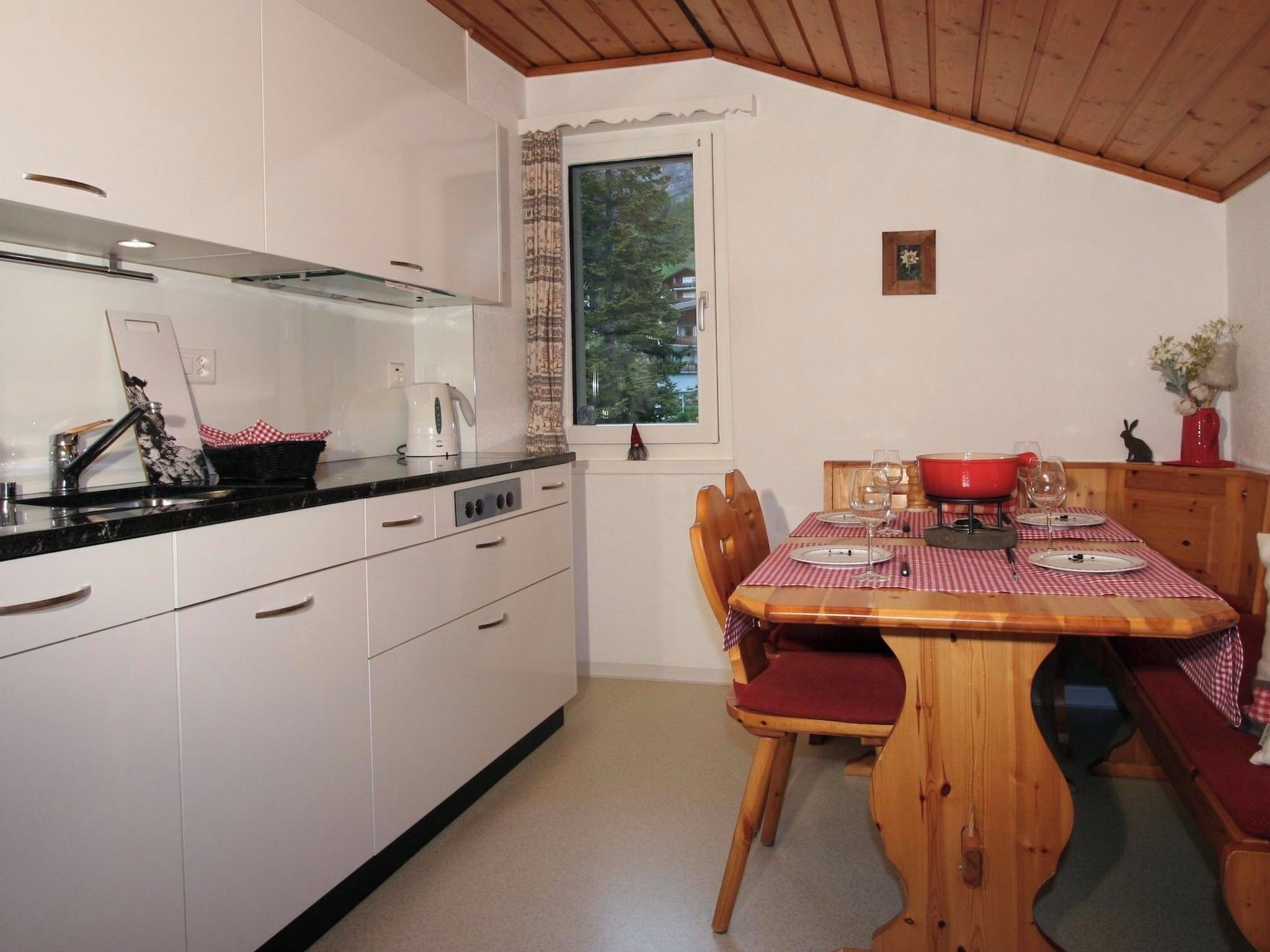 A compact kitchen with white cabinets, a black countertop, and a dining area with a wooden table and red chairs.