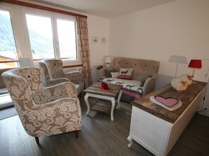 Ein gemütliches Wohnzimmer mit einer Couch, Sesseln, einem Couchtisch und einem kleinen Tisch mit einer Lampe.