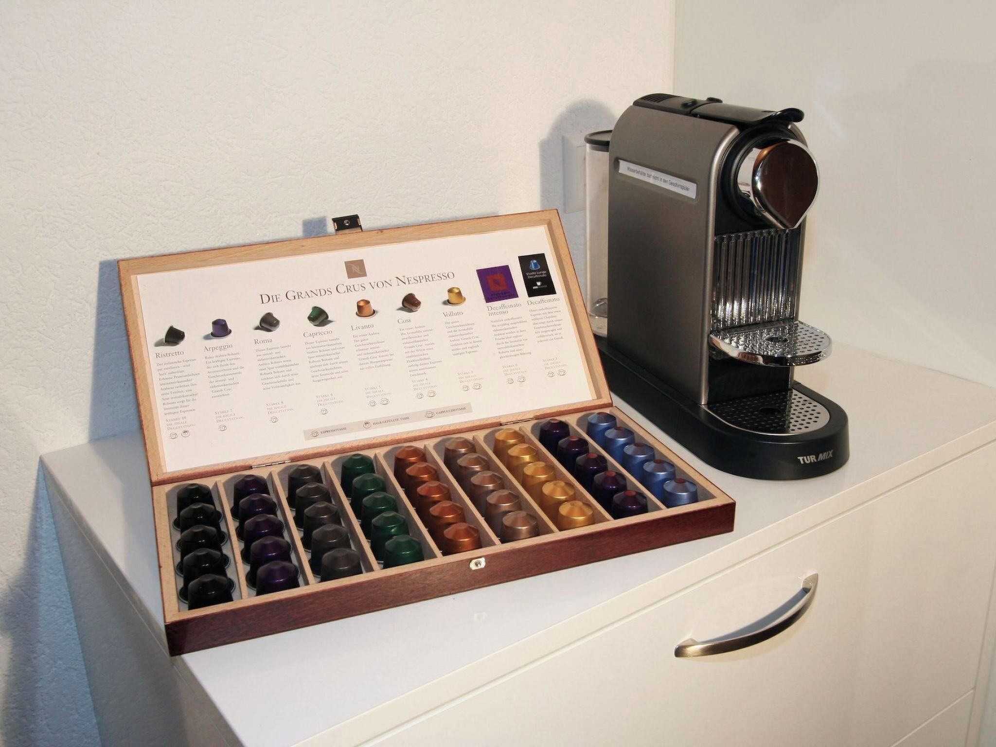Una máquina de café con un molinillo espresso manual y una selección de granos de café en una caja de madera.