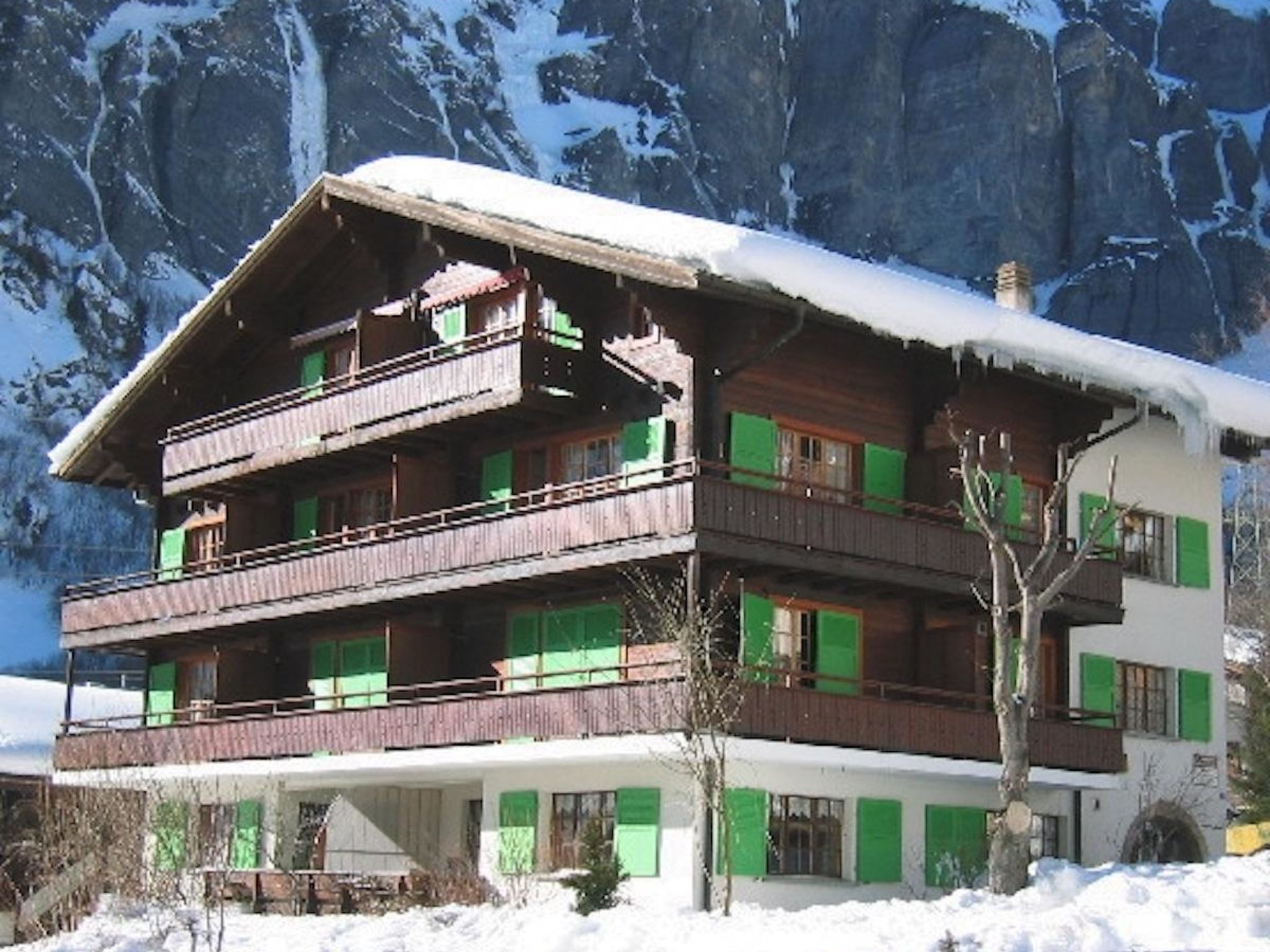 Ein mehrstöckiges Chalet mit Balkonen vor einer verschneiten Berglandschaft.