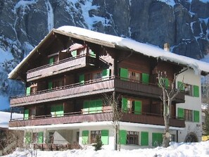 Ein mehrstöckiges Chalet mit Balkonen vor einer verschneiten Berglandschaft.