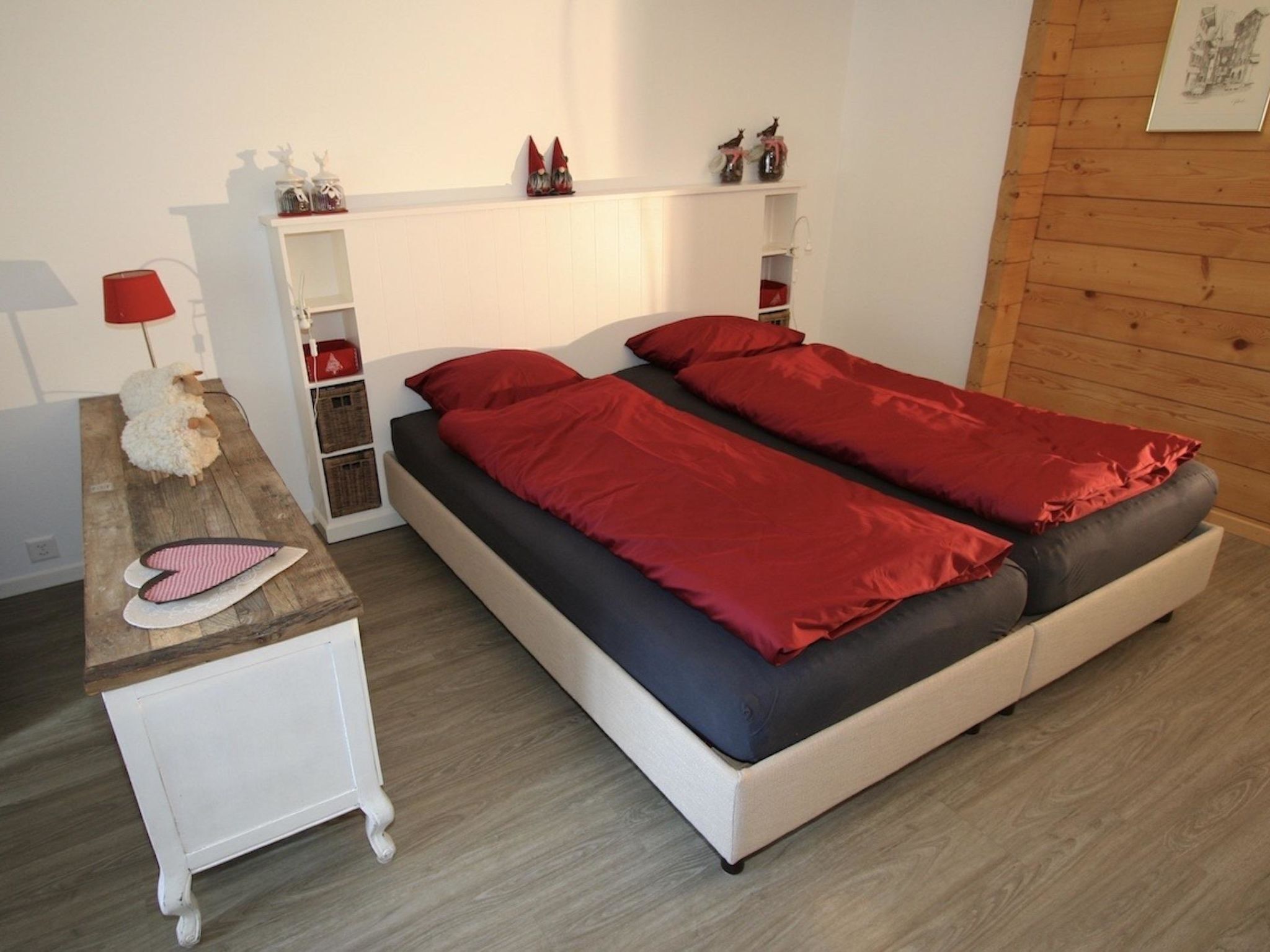 A bedroom with a bed, bedside tables, a lamp, and a shelf with decorative items.
