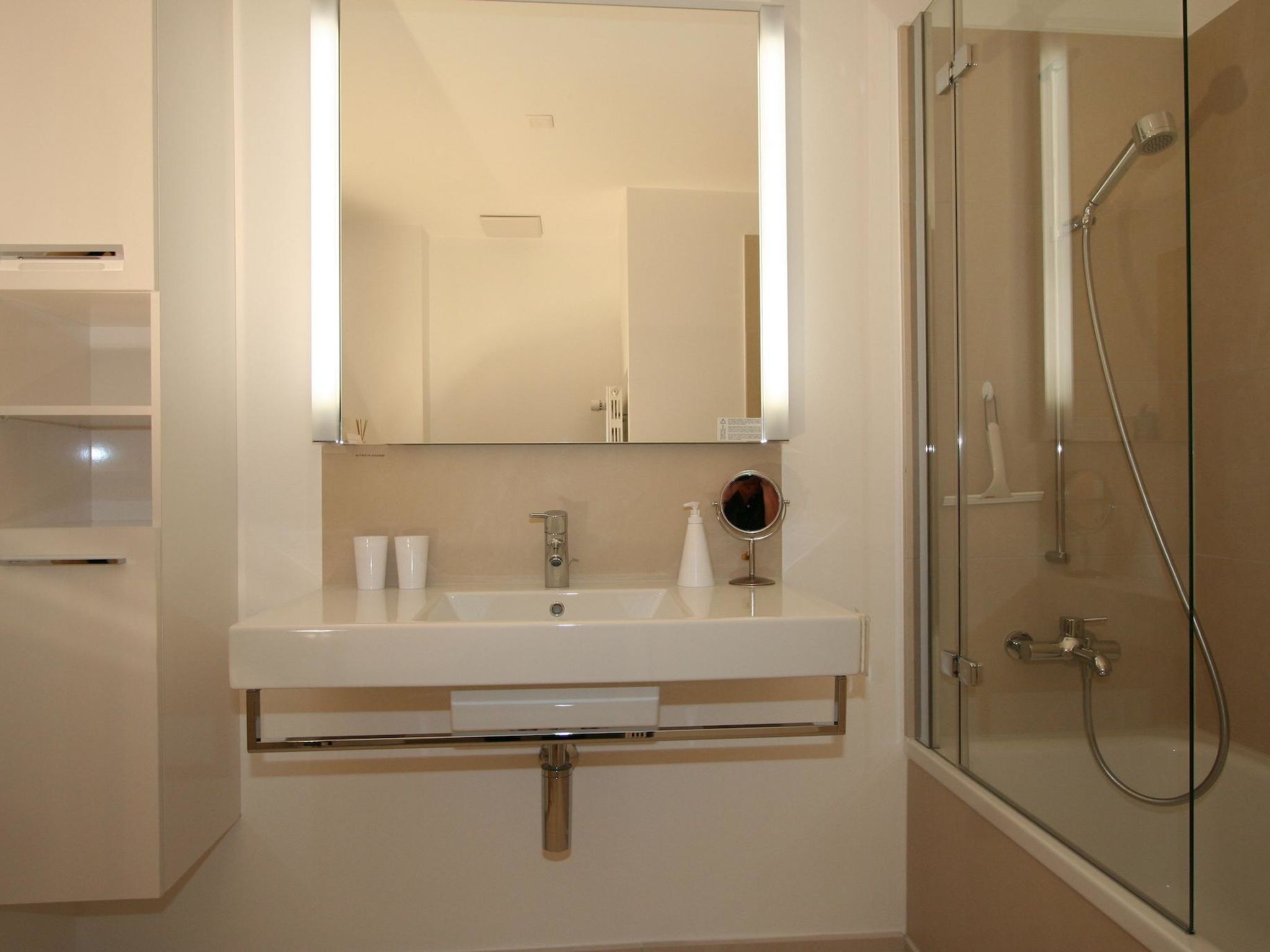 Un bany modern amb un mirall gran, un lavabo i una dutxa amb portes de vidre.