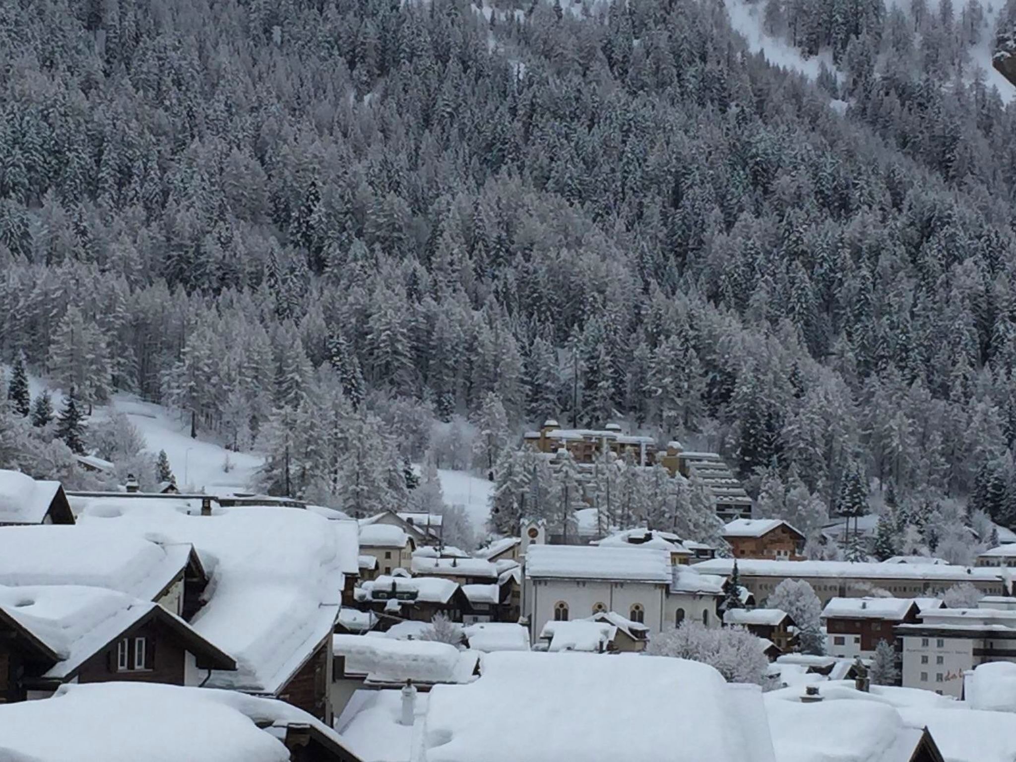 En snötäckt by med traditionella byggnader och en skogbeklädd bergskedja i bakgrunden.
