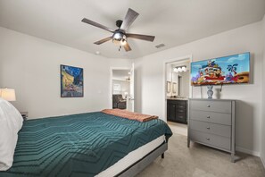 Une chambre à coucher avec un lit, un ventilateur de plafond, une commode, un téléviseur et un tableau accroché au mur.