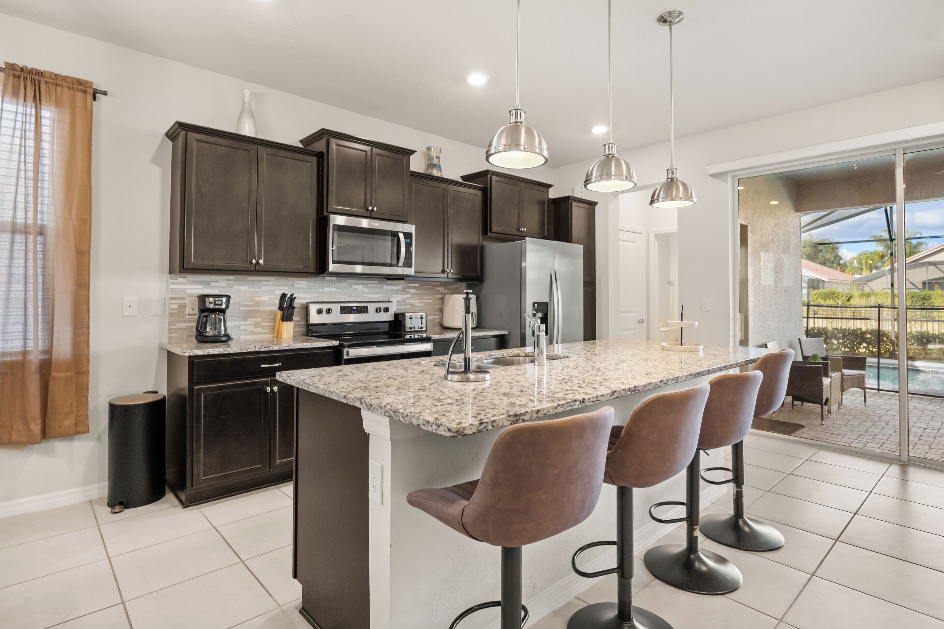 A modern kitchen with dark cabinets, stainless steel appliances, a granite countertop, and bar stools.