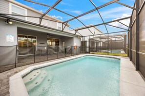 A covered swimming pool with a glass enclosure, a patio area with outdoor seating, and a view of a building with a sign. - 4039-Lana (Davenport)