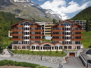 Ein mehrstöckiges Hotel mit Balkonen, einer Steinfassade und einem Bergpanorama im Hintergrund.