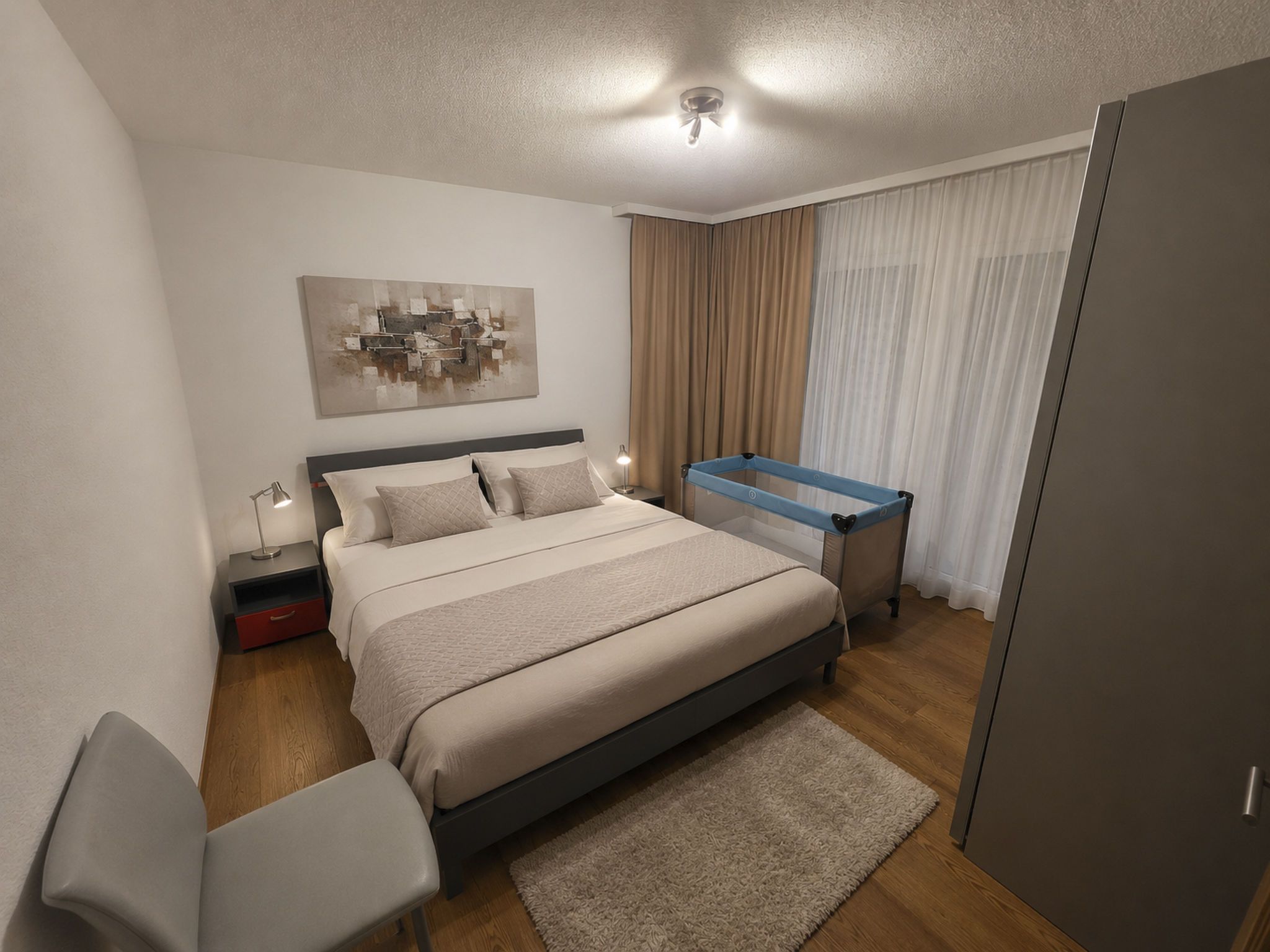 Ein modernes Schlafzimmer mit einem Bett, einem Nachttisch, einer Lampe und einem blauen Babybett.