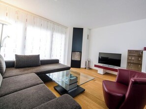 Ein modernes Wohnzimmer mit einer Couch, einem Glastisch, einem roten Sessel, einem Flachbildfernseher und einem Kamin.
