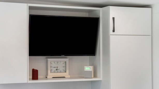 A white entertainment unit with a flat-screen TV, a clock, and a speaker. - Apartment 'Villa Wiese  Vineta' with Wi-Fi (Katzow)