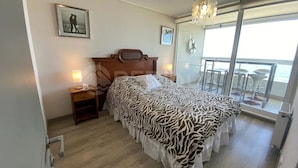 Un dormitorio con una cama estampada de cebra, lámparas de noche, un cuadro en la pared y un balcón con vistas.