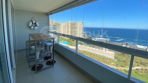 Un balcón con mesa y sillas, un flotador en la pared y vistas al océano y edificios.