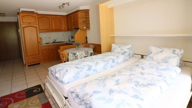 Habitación compacta con cama, una mesita y kitchenette.