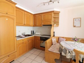 Eine kleine Küche mit Holzschränken, einem eingebauten Ofen und einer Essecke mit einer Bank.