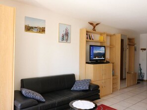 A living room with a black leather sofa, a television on a wooden cabinet, and a small round table with a white object on it. - Adlerhorst Leukerbad # 2-bed apartment, Dusche, WC by Interhome (Leukerbad)