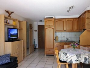 Ein kompakter Wohnbereich mit Küchenzeile, einem Essbereich mit Tisch und Stühlen, einem Fernseher auf einem Regal und Holzschränken.