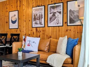 Eine holzgetäfelte Wand mit gerahmten Fotografien, ein braunes Ledersofa mit Kissen und ein kleiner Tisch mit einer Pflanze.