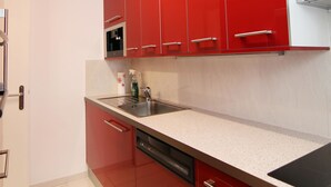 A kitchen with red cabinets, a stainless steel sink, and a dishwasher. - Viktoria B16 by Arosa Holiday Appartement/Fewo, Dusche oder Bad, WC, 4-Bettwohnu by Interhome (Arosa)