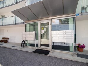 Une entrée moderne avec des portes en verre, un banc, un porte-vélos et un pot de fleurs.