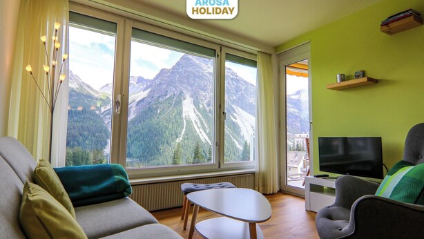 A modern living room with a mountain view, a sofa, a table, a chair, and a television. - Viktoria B16 by Arosa Holiday Appartement/Fewo, Dusche oder Bad, WC, 4-Bettwohnu by Interhome (Arosa)
