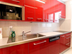 Une cuisine moderne avec des meubles de rangement rouges, des appareils électroménagers en acier inoxydable et un lave-vaisselle.