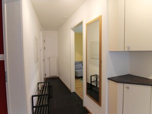 Un couloir avec un radiateur, une porte et un aperçu d’une pièce où se trouve un lit.
