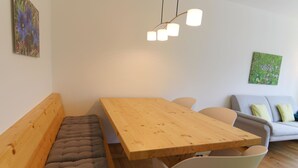 A modern living space with a wooden dining table, cushioned bench seating, a sofa, and a hanging light fixture. - Viktoria B16 by Arosa Holiday Appartement/Fewo, Dusche oder Bad, WC, 4-Bettwohnu by Interhome (Arosa)
