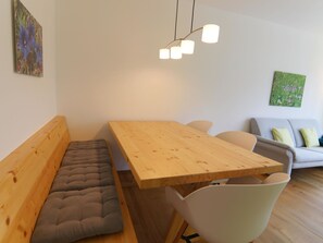 Ett modernt vardagsrum med ett matbord i trä, en bekväm bänk, en soffa och en hängande lampa.