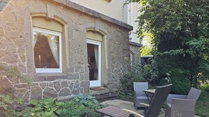 Ein Steinhaus mit einer kleinen Terrasse, ausgestattet mit Korbmöbeln und einem Garten.