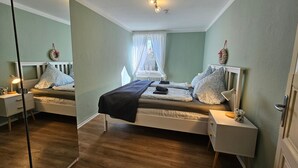 Ein Schlafzimmer mit einem Bett, Nachttischen, einem Spiegel und einem Fenster mit Vorhängen.