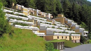 Un barrio residencial en una ladera con casas modernas, una carretera y un bosque denso al fondo.