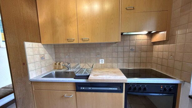 Una cocina compacta con armarios de madera, lavavajillas integrado y estufa.