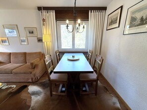 Uma sala de jantar com mesa e cadeiras, um lustre, um sofá e uma janela com cortinas.