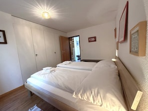 A bedroom with a bed, a wardrobe, and a door leading to another room. - Lärchenwald 1808 # 4-bed apartment, Bad, WC 4-Bettwohnung, Bad, WC by Interhome (Leukerbad)