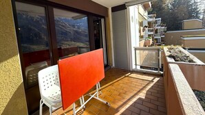 Un balcón con una silla blanca, una mesa roja y vistas a la montaña.